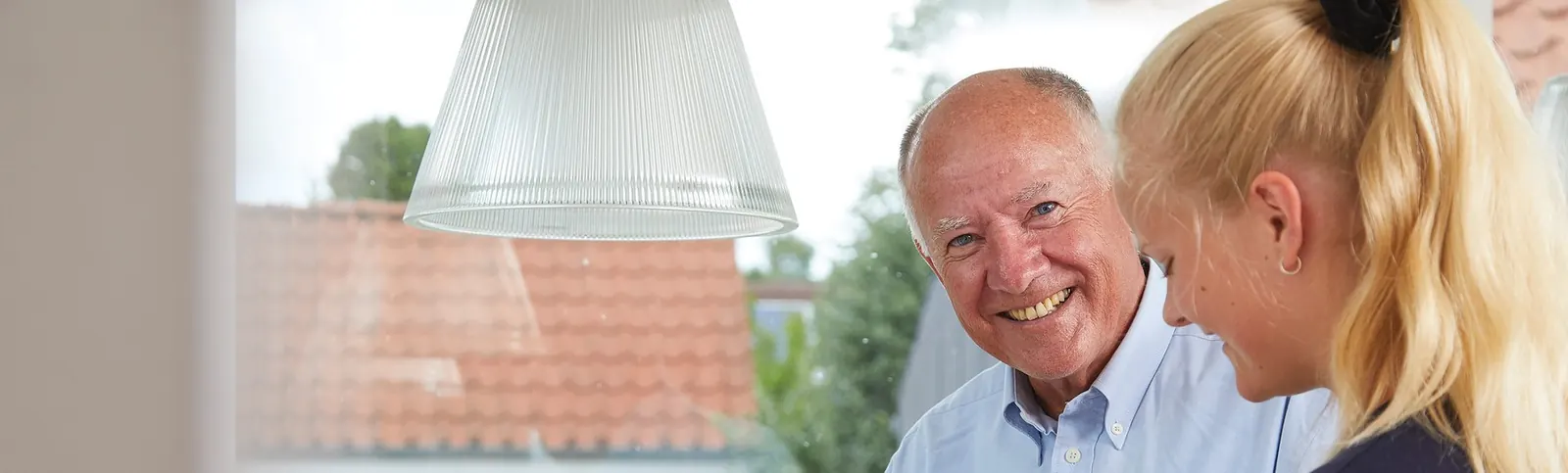 An older client and a care worker share a smile at home in Denmark