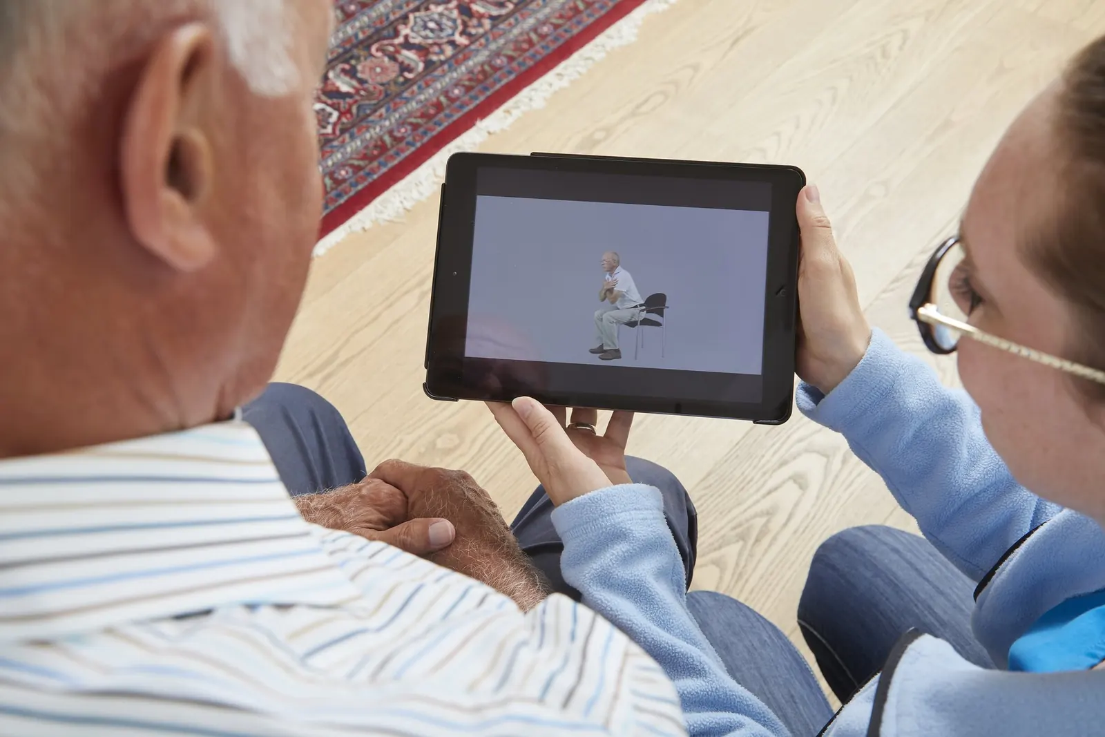 A care worker shows an older client an exercise on the tablet